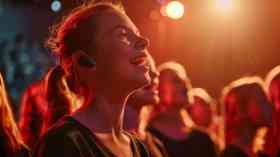 A girl wearing a hearing aid sings in a choir.
