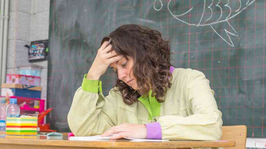 Teacher looks tired at a desk.