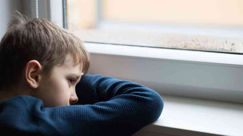 Sad young boy looks out of window.
