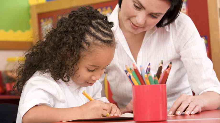 Young girl drawing while teacher watches.