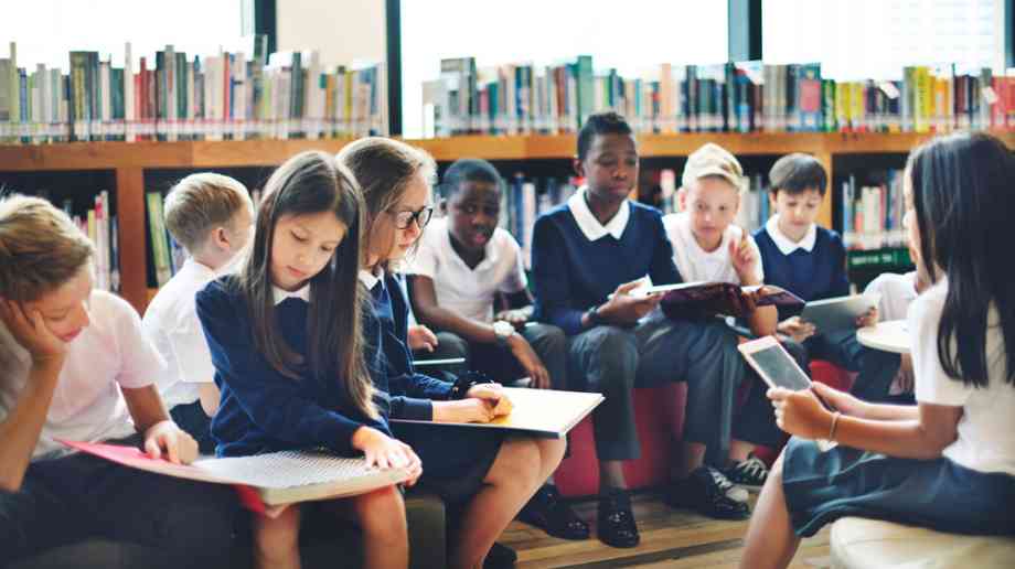 School children in uniform sit in library reading