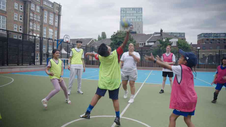 Six children play with a ball on a court with a coach.